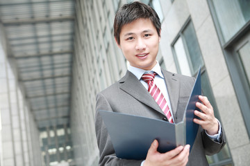 a yong Asiatic businessman  is reading document outdoor