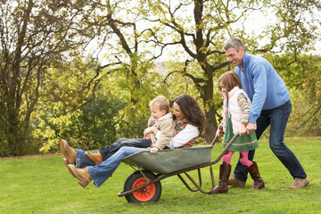 Family With Man Giving Mother And Children Ride In Wheelbarrow
