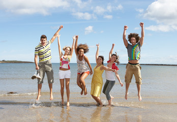 Group Of Teenage Friends Having Fun On Beach Together Jumping In