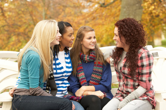 Group Of Four Teenage Girls Sitting And Chatting On Bench In Aut