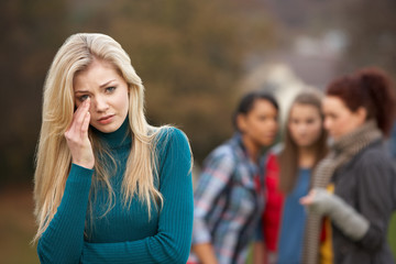Upset Teenage Girl With Friends Gossiping In Background