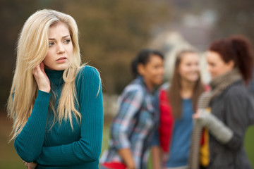 Fototapeta na wymiar Upset Teenage Girl With Friends Gossiping In Background