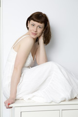 Obraz na płótnie Canvas flirting woman in white dress sitting on chest of drawers