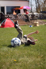 Obraz premium Little boy falling down on grass while playing ball