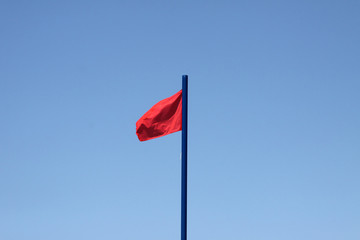 Czerwona ostrzegawcza flaga na plaży na niebieskim niebie © wideonet