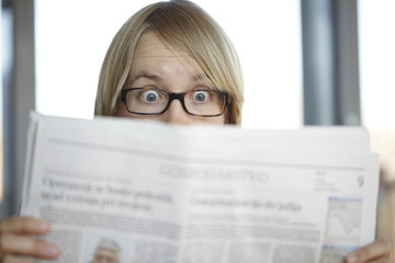 Surprised woman with glasses reading a newspaper in shock - 22385225