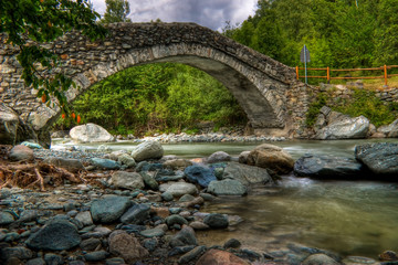 Fototapeta na wymiar Ponte romano su torrente di pietre in alta montagna