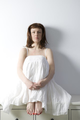 flirting woman wearing white dress sitting on chest of drawers