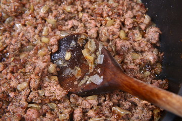 Minced meat and onion being fried on a pan and a ladle