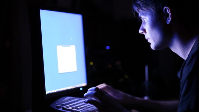 Young man in front of computer screen. Dark night room.
