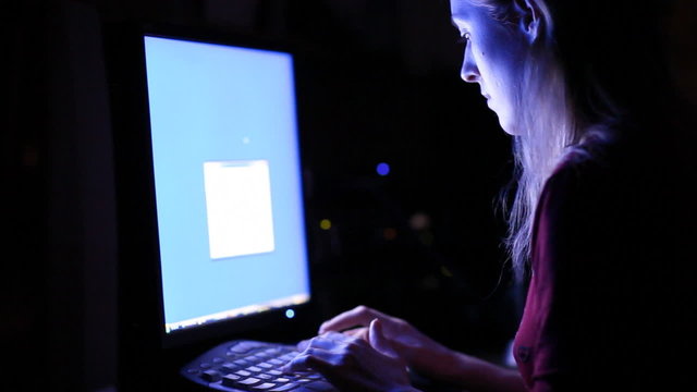 Young woman in front of computer screen. Dark night room.