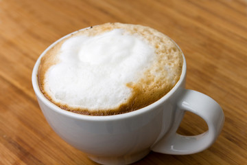 Cappuccino with froth in white cup  on wooden table.