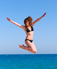 young beautiful woman jumps against the sea