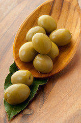 green olives over the spoon on wood background