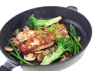 fried fish with vegetables in a black pan isolated on white