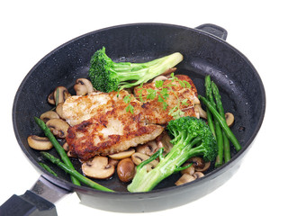 fried fish with vegetables in a black pan isolated on white
