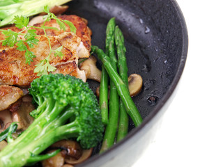 fried fish with vegetables in a black pan isolated on white