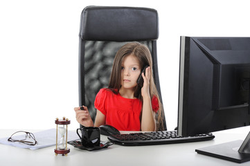 Little girl talking on the phone at the table in front of a comp