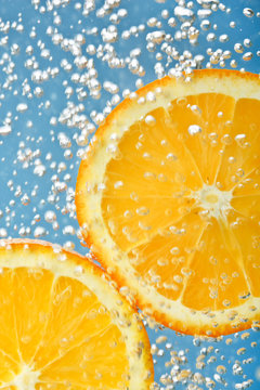 Fresh orange dropped into water with bubbles.