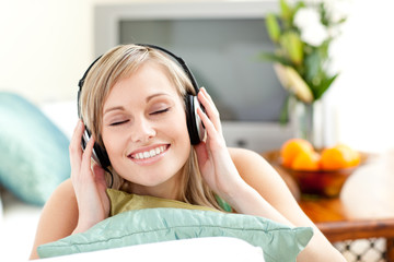 Naklejka premium Delighted young woman listening music lying on a sofa
