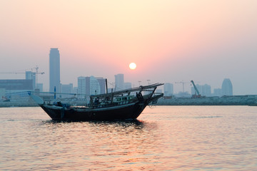Bahrain city silhouette and fishing dhow in sunset