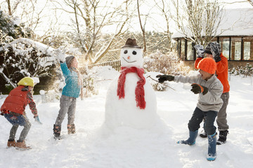 Mother And Children Building Snowman In Garden