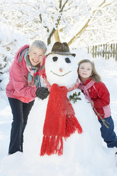 Young Girl With Grandmother Building Snowman In Garden