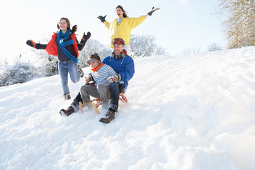 Fototapeta na wymiar Family Having Fun Sledging Down Snowy Hill