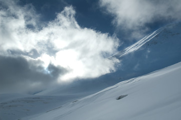 Fototapeta na wymiar Sun shining through the cloud covering snowy cracked slope.
