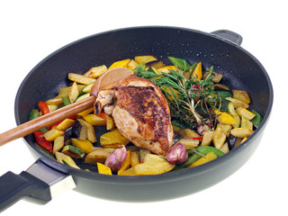 fried chicken & vegetables in a black pan isolated on white