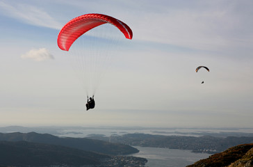 Two paragliders flying over Norwegian coastal landscape