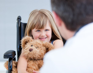 Smiling little girl sitting on the wheelchair with her teddy bea