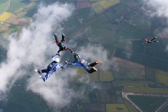 Three skydivers in freefall with a fourth one below them