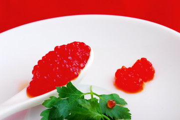 Spoon with red caviar and greens parsley on a white plate