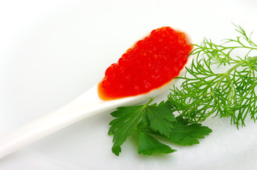 Spoon with red caviar and greens parsley on a white plate
