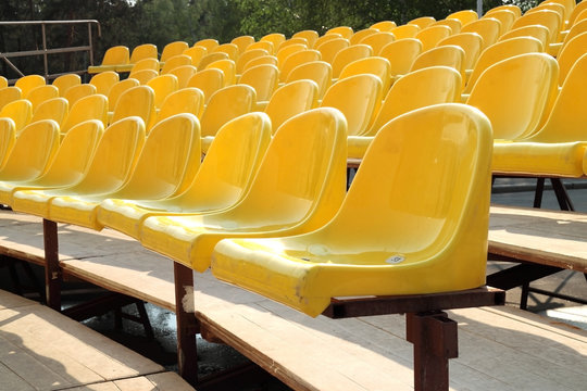Empty rows of yellow plastic chairs on wooden scaffold
