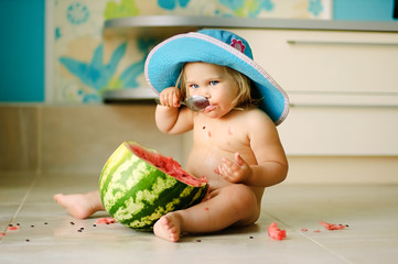 Cute baby-girl in a hat and eats a water-melon with a spoon