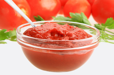 Ketchup in glass dish on background of red tomatos
