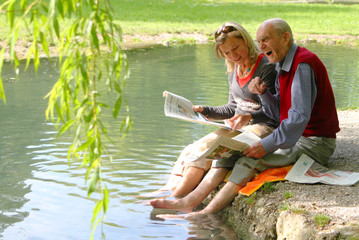 Großvater und Enkelin beim Zeitunglesen im Grünen am Teich