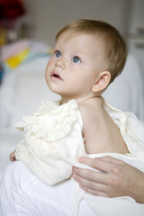 Fototapeta premium Cute baby sitting on a bed dressed in a bodysuit