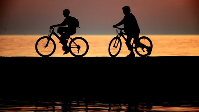 Silhouettes of two cyclists at sunset in the sea.