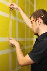worker man measuring interior wall with masking tape
