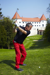Man hitting a golf ball on the golf course with a castle