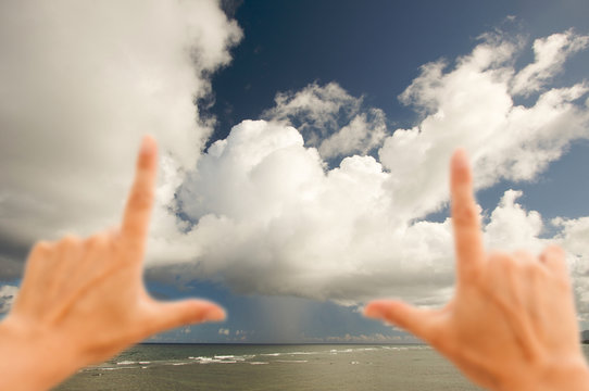 Hands Framing Dramatic Clouds over Tropical Shoreline