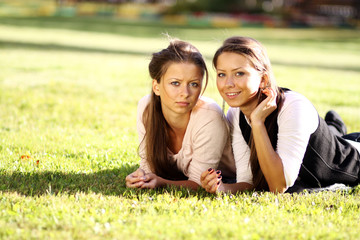 Young beautiful twins of sister lays on green field