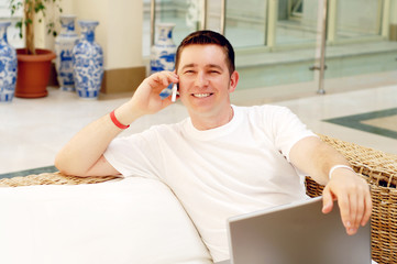 Smiling young man working on laptop computer and call by phone a