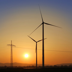 Windräder und Strommast im Sonnenuntergang