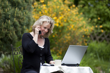 hübsche blonde Frau mit Mobiltelefon und Laptop im Grünen