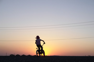 Girl rides bicycle in sunset