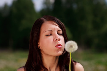 The girl blows on a dandelion on a background of a grass